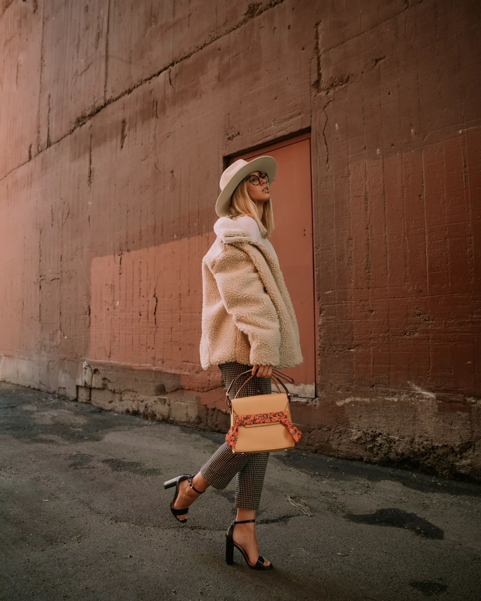 Portrait of a woman walking beside a textured peach wall.