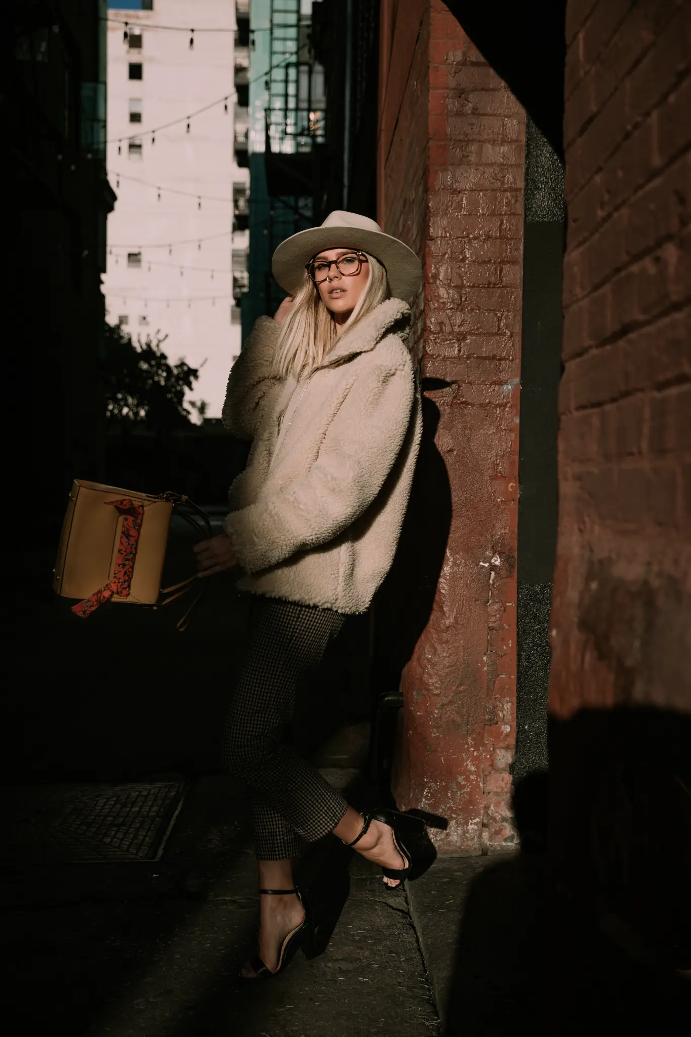 Full-length city portrait of a woman in a light coat and hat.