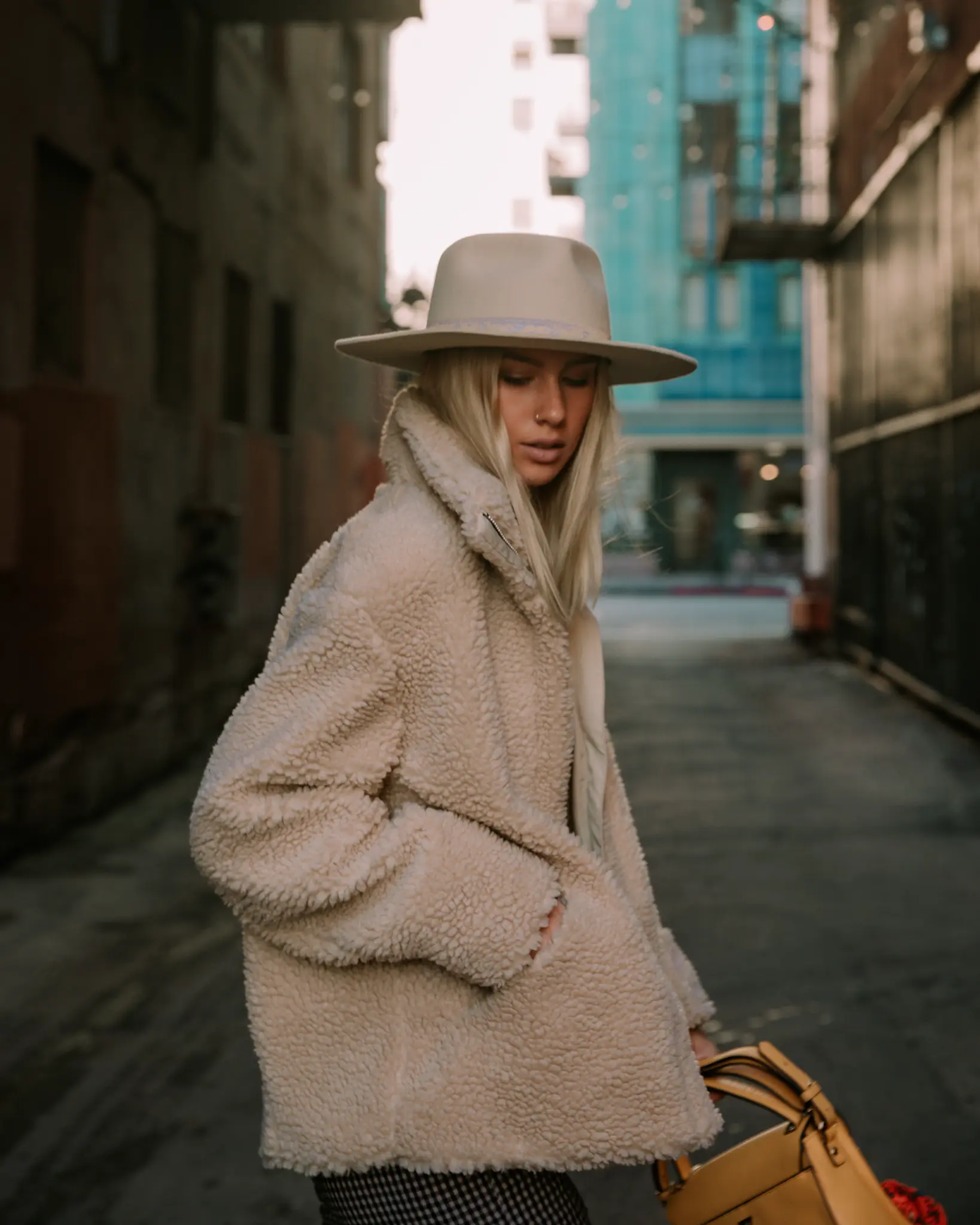 Portrait of a woman in a light coat and hat in a city alley.