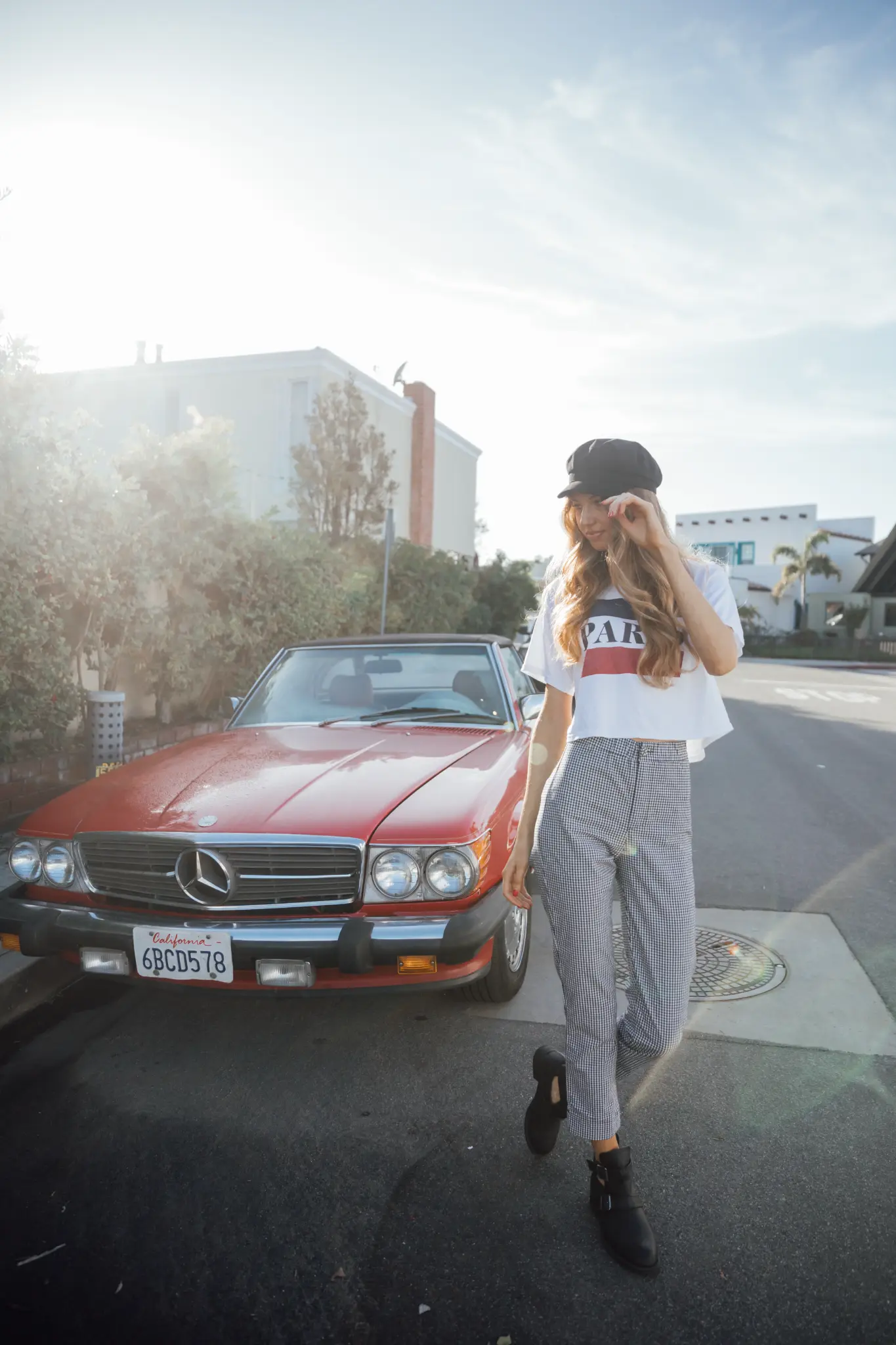 Woman standing beside a red vintage car on a sunny street.