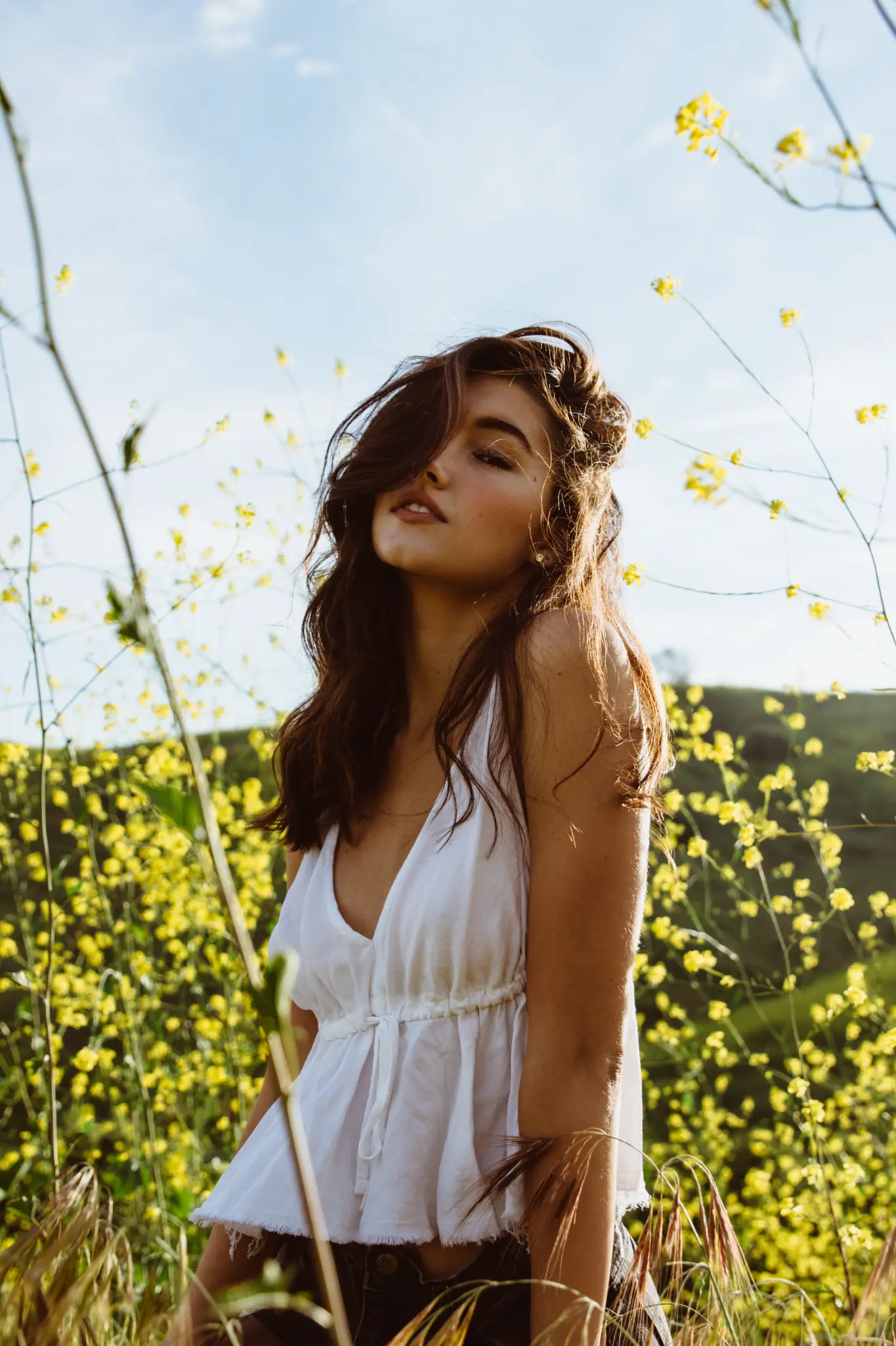 Sunlit portrait of a woman in a field of yellow flowers.